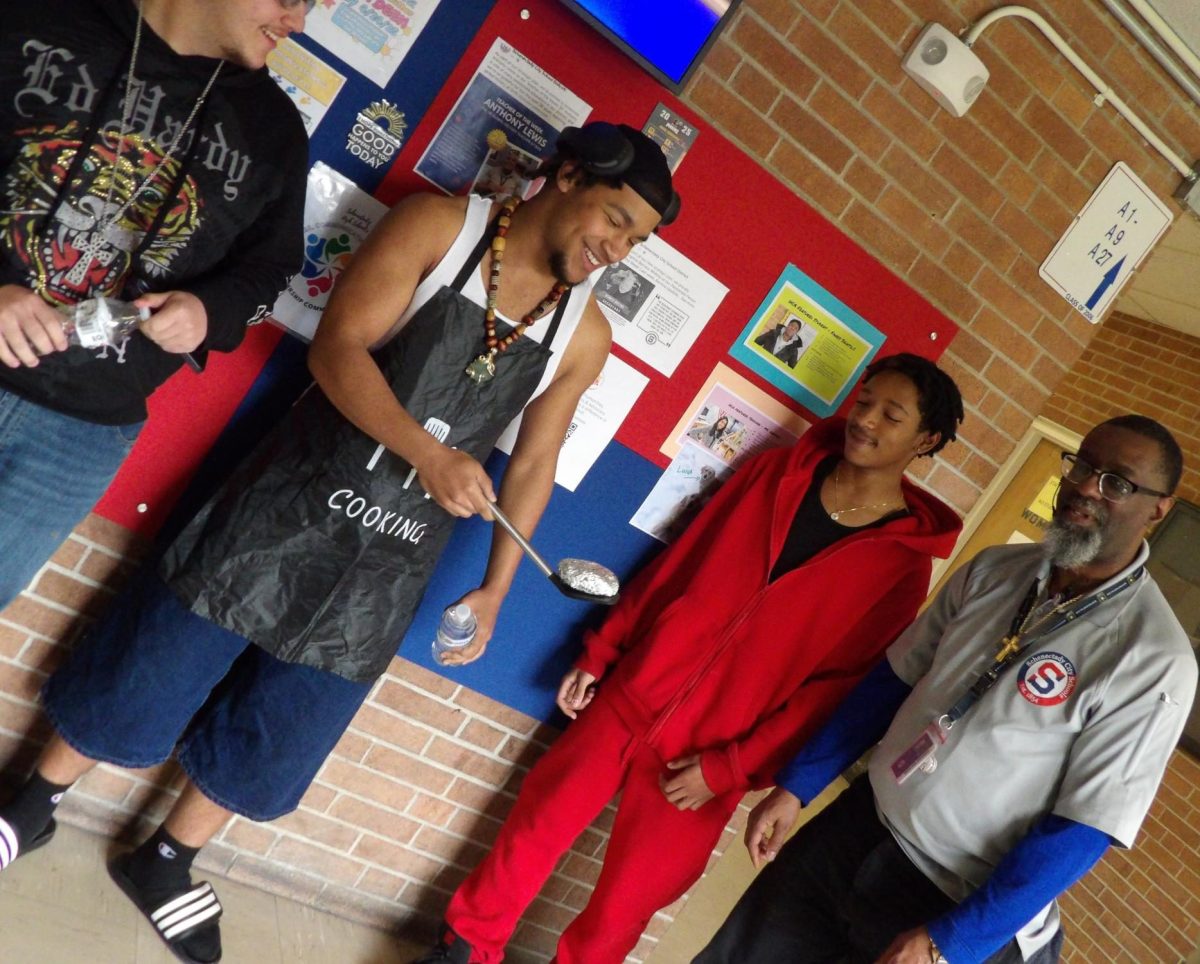 Students talk in the halls with Mr. Henderson. In order from left-to-right, are Evian Velez, Mujahid Al-Kabir, Treshawn Perrin, and Mr. Henderson.